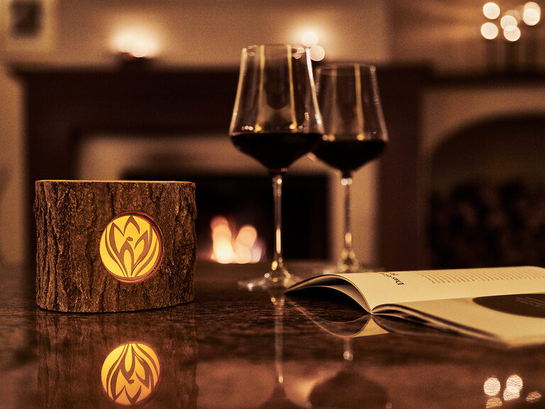 Der Kamin in der Bar & Lounge im Hotel Kronelamm sorgt für gemütliche Stunden an kalten Wintertagen. Zwei Gläser Rotwein stehen auf einem Tisch vor einem angefeuerten Kamin