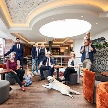 Members of the Berlin family sit and stand in a lounge decorated with gray and orange furniture.