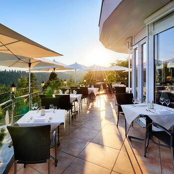 Eingedeckte Tische und Stühle bei strahlendem Sonnenschein auf der Terrasse des Hotelrestaurantsestaurants.