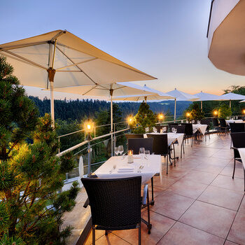 Eingedeckte Tische mit Stühlen aus der Terrasse mit Sonnenuntergang.