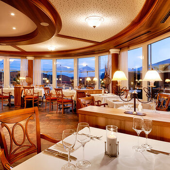 A round room with panoramic windows through which you can see the dusk and tables set for the evening meal.