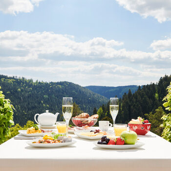 Ein reichlich gedeckter Frühstückstisch auf der Restaurantterrasse mit Blick auf den Schwarzwald im Hintergrund