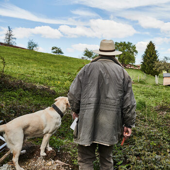 Rolf Berlin und sein weißer Labrador stehen bei blauem Himmel auf einer grünen Wiese und schauen in die Ferne.