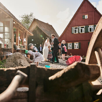 A groom and a bride are standing in the middle of the Theurerhof estate with lots of guests in the background.