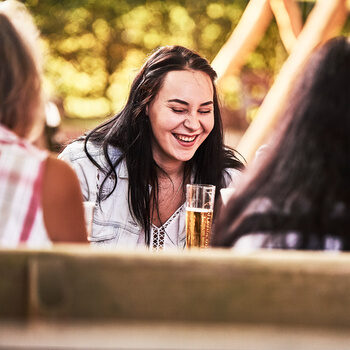 Drei Damen sitzen im Biergarten im Wanderheim Zavelstein an einen großen Tisch und unterhalten sich.