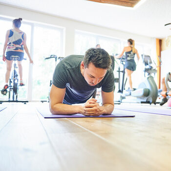 Ein junger Gast trainiert im Ellbogenstütz auf einer Sportmatte in einem Fitnessraum.