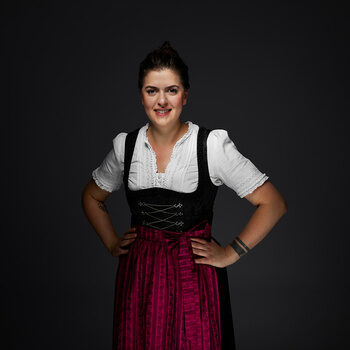 Veranstaltungsleiterin, Tugba Aslan, im Dirndl bekleidet vor einem dunklen Hintergrund.