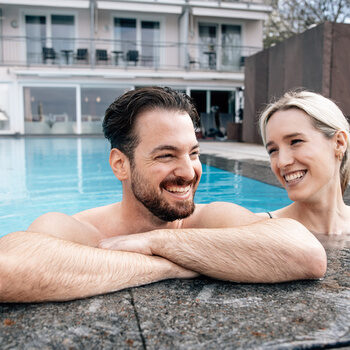 Ein gut gelauntes Paar entspannt zusammen in einem  Aussenpool des Wellnesshotels Kronelamm