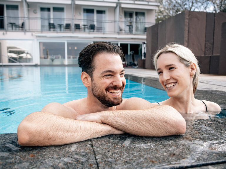 Ein gut gelauntes Paar entspannt zusammen in einem  Aussenpool des Wellnesshotels Kronelamm