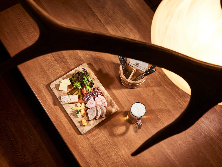 Das Wanderheim von Familie Berlin bietet unter anderem rustikale Speisen an. Auf einem Vesperbrett sind verschiedene Wurstsorten, Käse, Salat, Butter und Brot angerichtet.
